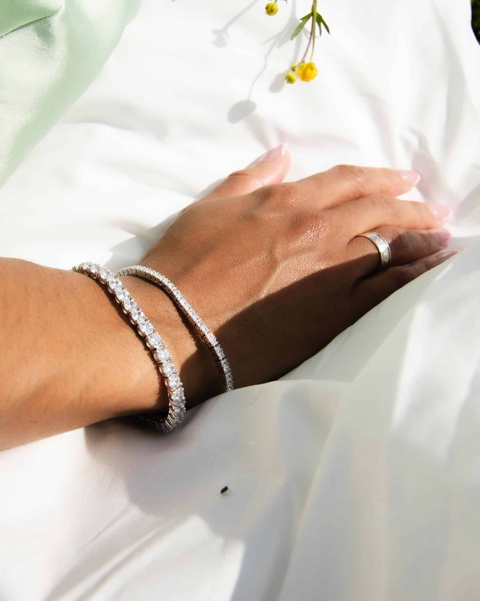 En kvinna bär på två tennisarmband från kagami, ett tunnare och ett tjockare. Hon har hennes hand vilande mot en vit klänning.