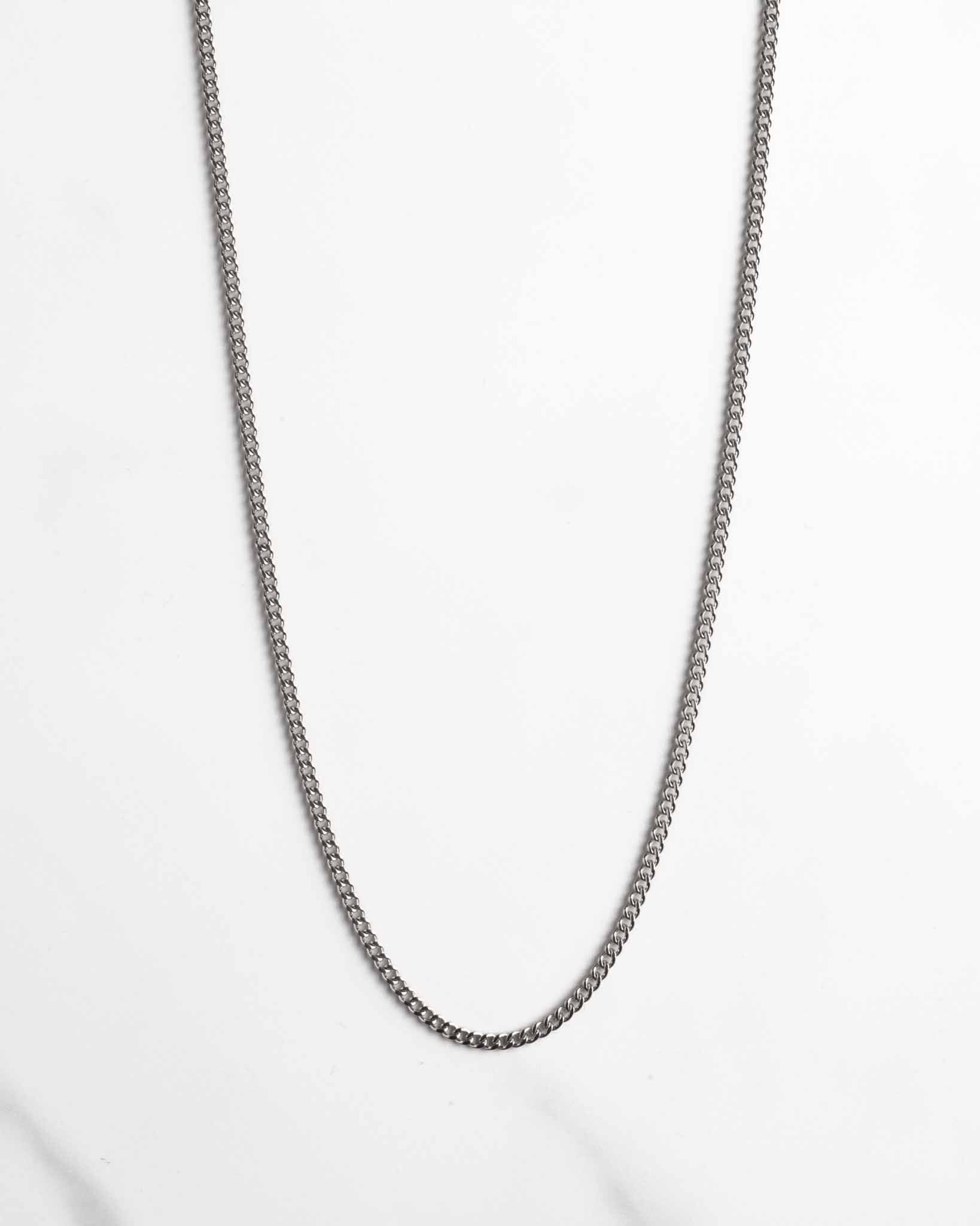 Ett enkelt Pansar halsband silver 2 mm kedjehalsband är utlagt i en lös kurva på en vit marmoryta.