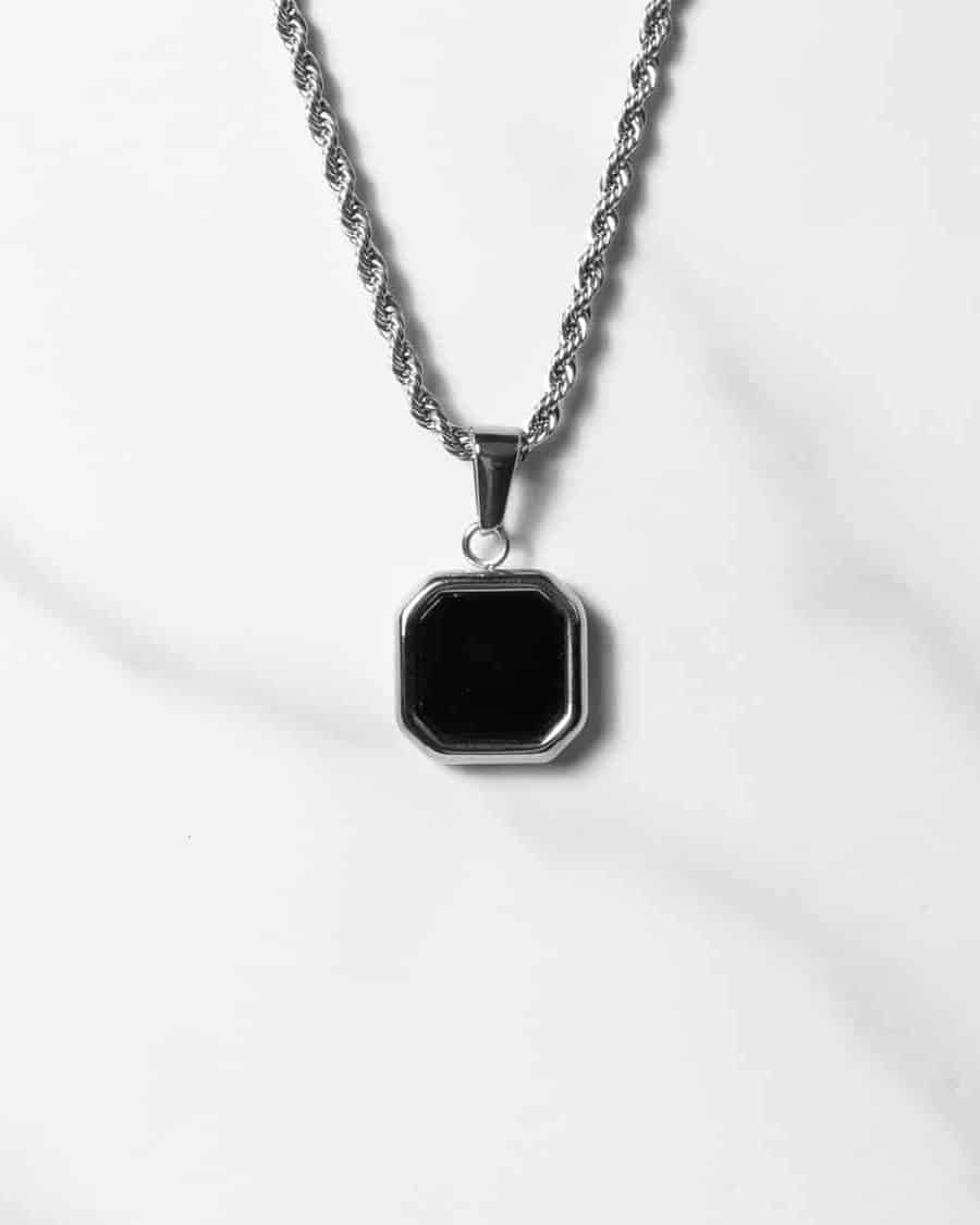 Ett halsband i silver med ett åttkantigt hänge i svart onyx, placerat på en vit marmoryta.