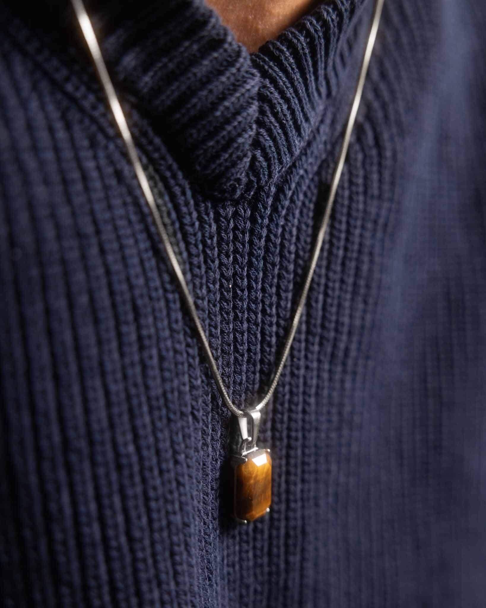 Närbild av Tiger Eye Silverhalsbandet med rektangulärt brunt ädelstenshänge, buret över en mörkblå ribbstickad tröja.