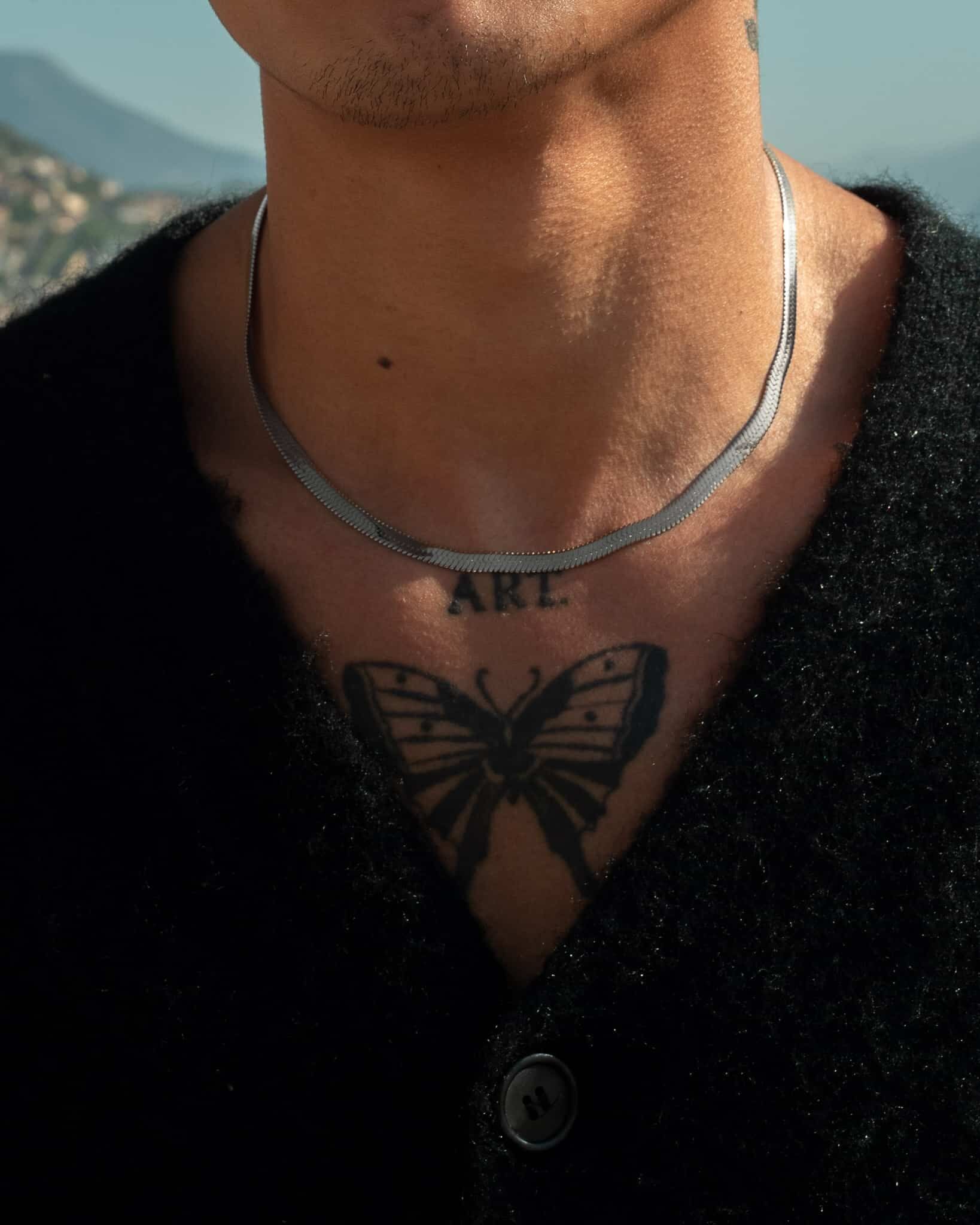 Person i svart kofta med Herringbone silver 5mm halsband med en suddig stadsbakgrund