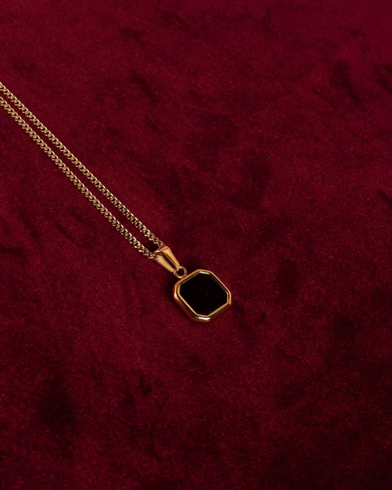 Pansarlänk 2mm guldsmycke med ett black onyx sten vilar mot en röd bakgrund