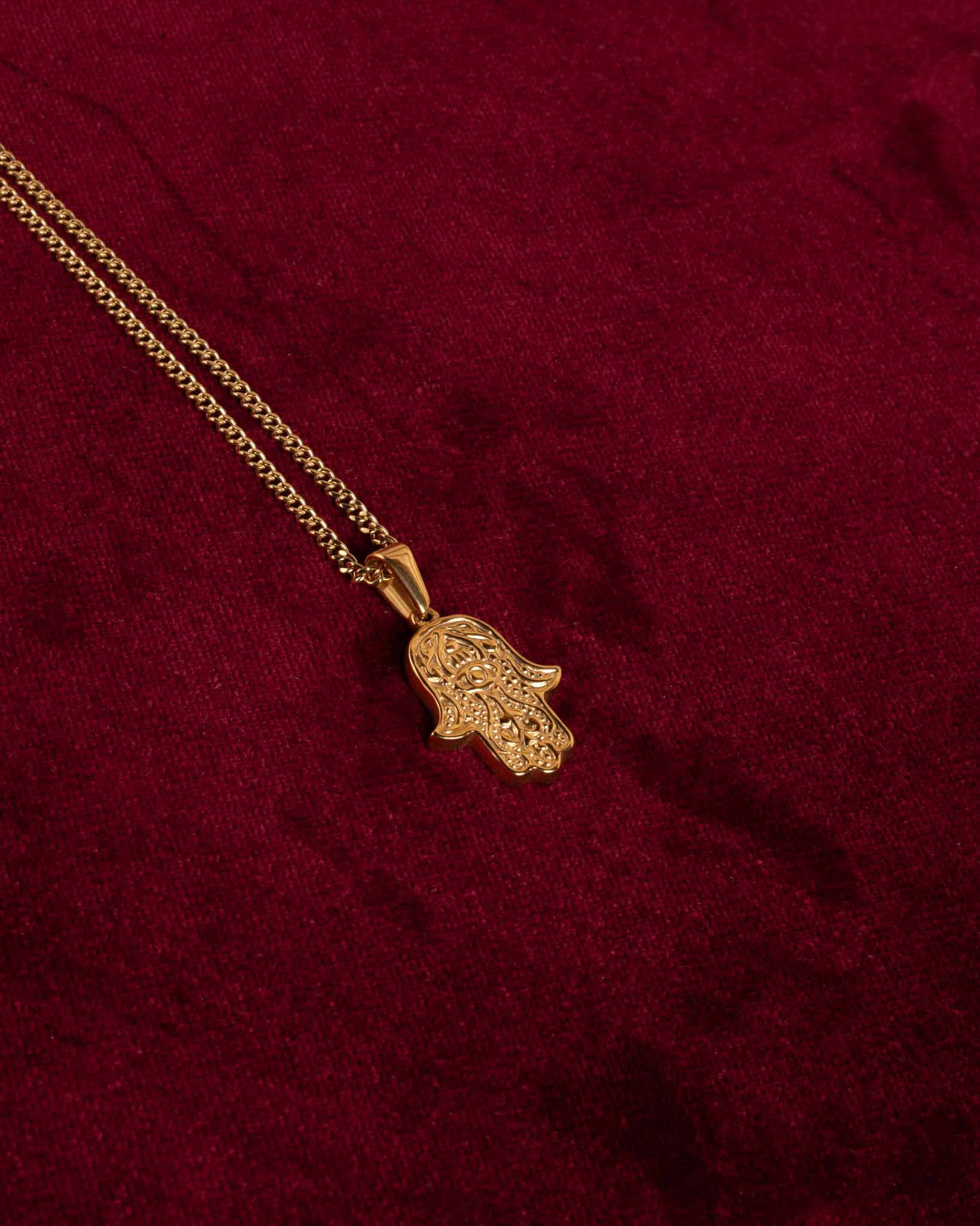 Ett guldigt hängsmycke med fathimas hand hängandes på en tunn guld kedja