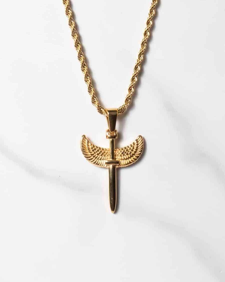 Ett guldhalsband med repkedja och ett Sword Guld-hänge i form av ett vertikalt svärd med utsträckta vingliknande detaljer på vardera sidan, mot en bakgrund av vit marmor.